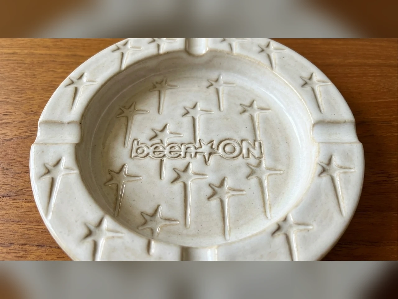 White ceramic been ON ashtray with raised lettering and star motifs on a wooden surface